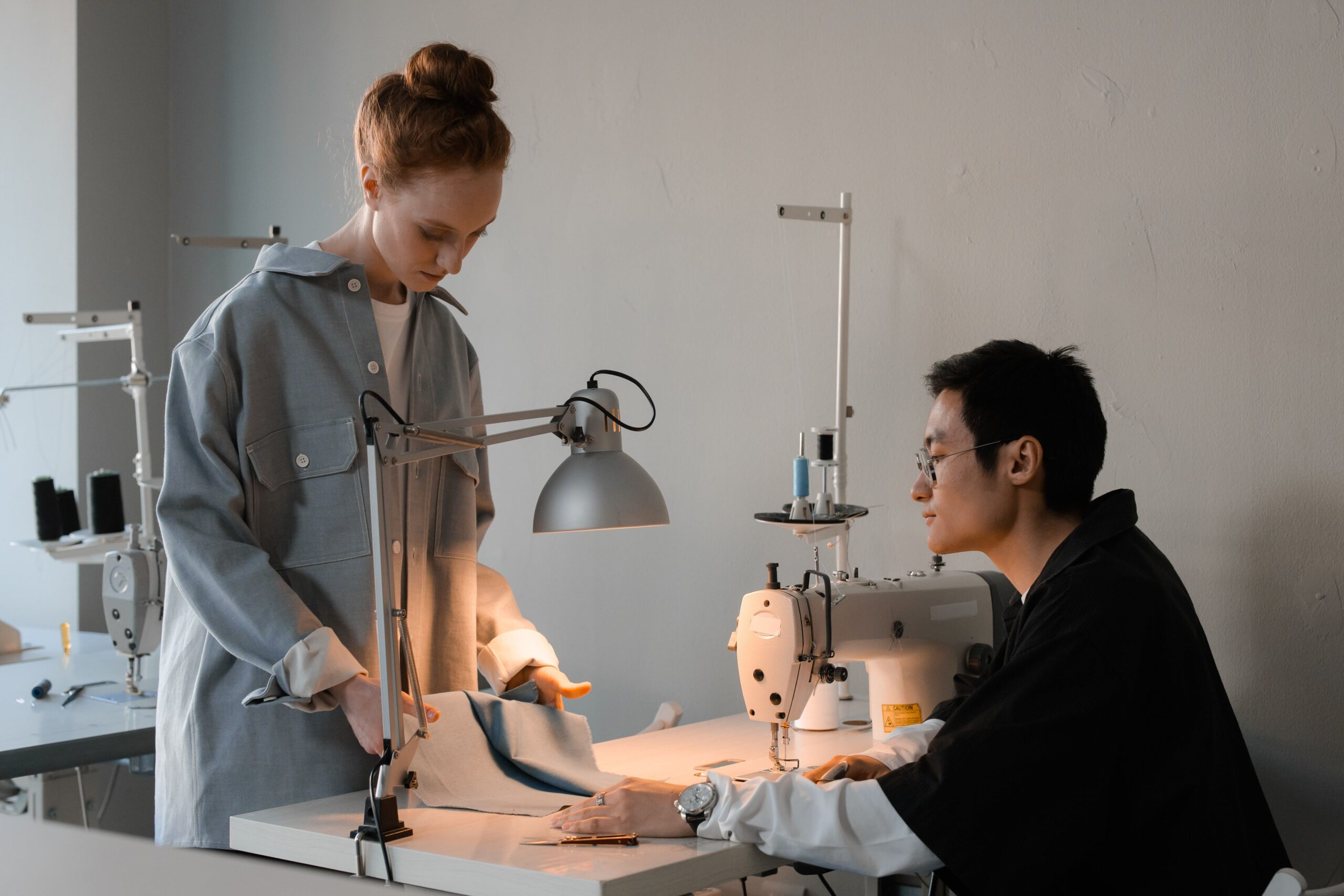 Two people reviewing fabric beside industrial sewing machines